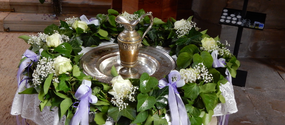 Taufstein geschmückt mit Blumen und Kelch in der Mitte